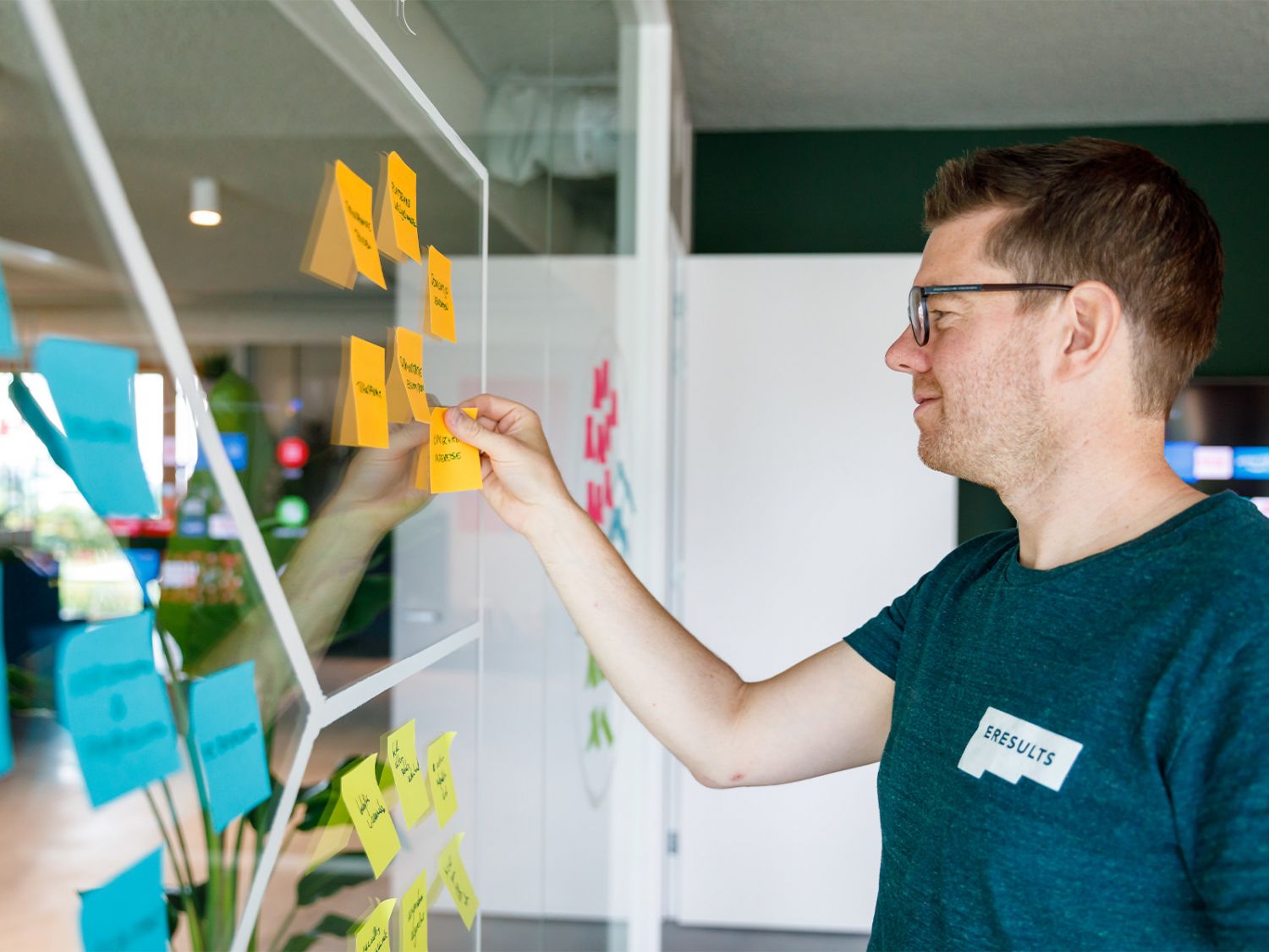 Pier plakt post-its over een merk op een glazen wand